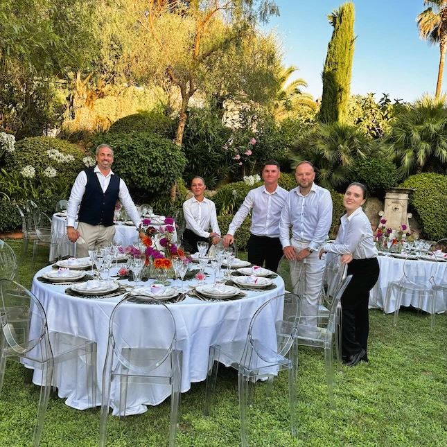 L'équipe de Mondello Hospitality lors d'un service haut de gamme. Une réception dans les jardins au milieu des tables, couverte de longues nappes blanches, dressées avec élégance et fleuries, n'attendent plus que les invités. Une réalisation dans l'esprit de Mondello Hospitality